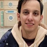 Portrait of a man wearing a hoodie and jacket indoors.